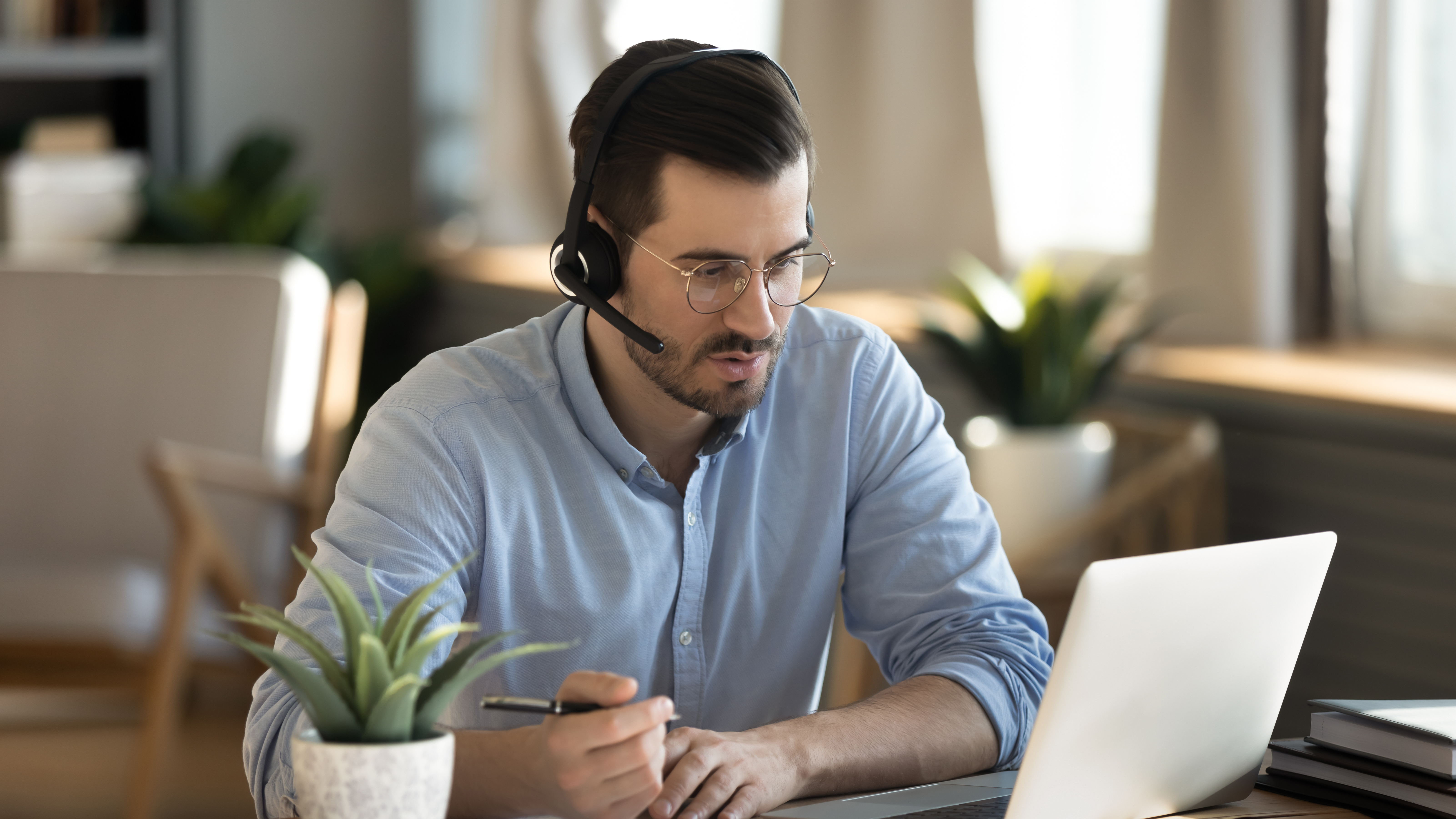 Focused man wearing headset writing notes, studying online